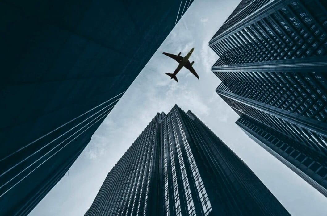 An airliner flying over city skyscrapers.