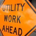 A utility work ahead sign near a job site using trenchless technology.